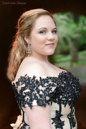 Fair skinned girl shown from the waist up in a pink dress with black overlay and lace trim with off the shoulder sleeves and a plunging neckline